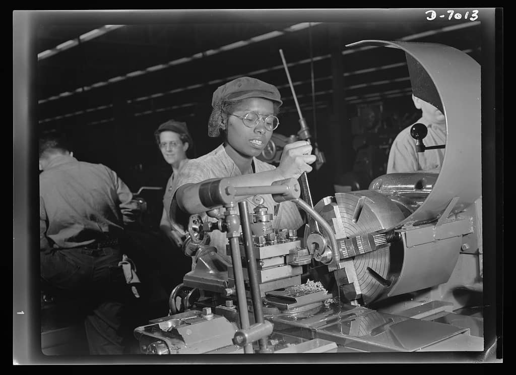 Annie Tabor at the lathe machining aircraft engine parts in 1942, two foremen looking on
